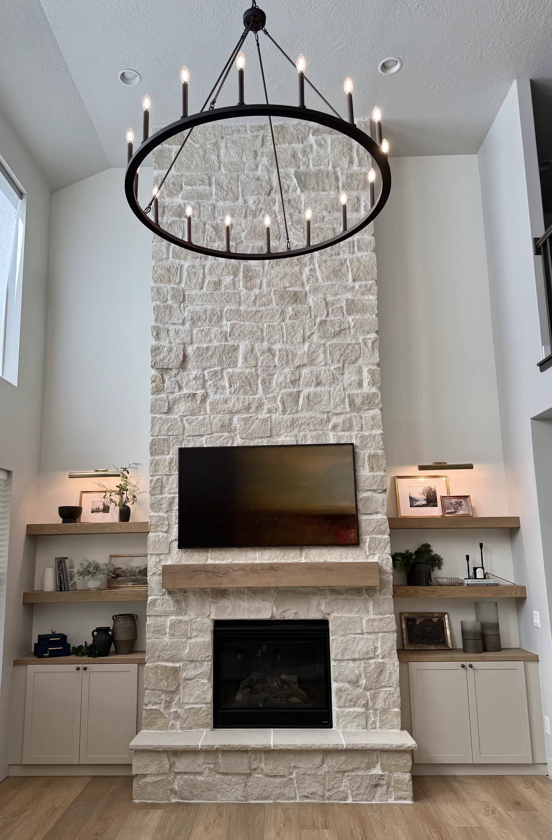 Two-story stone fireplace with floating shelves and chandelier by BK Toolbox