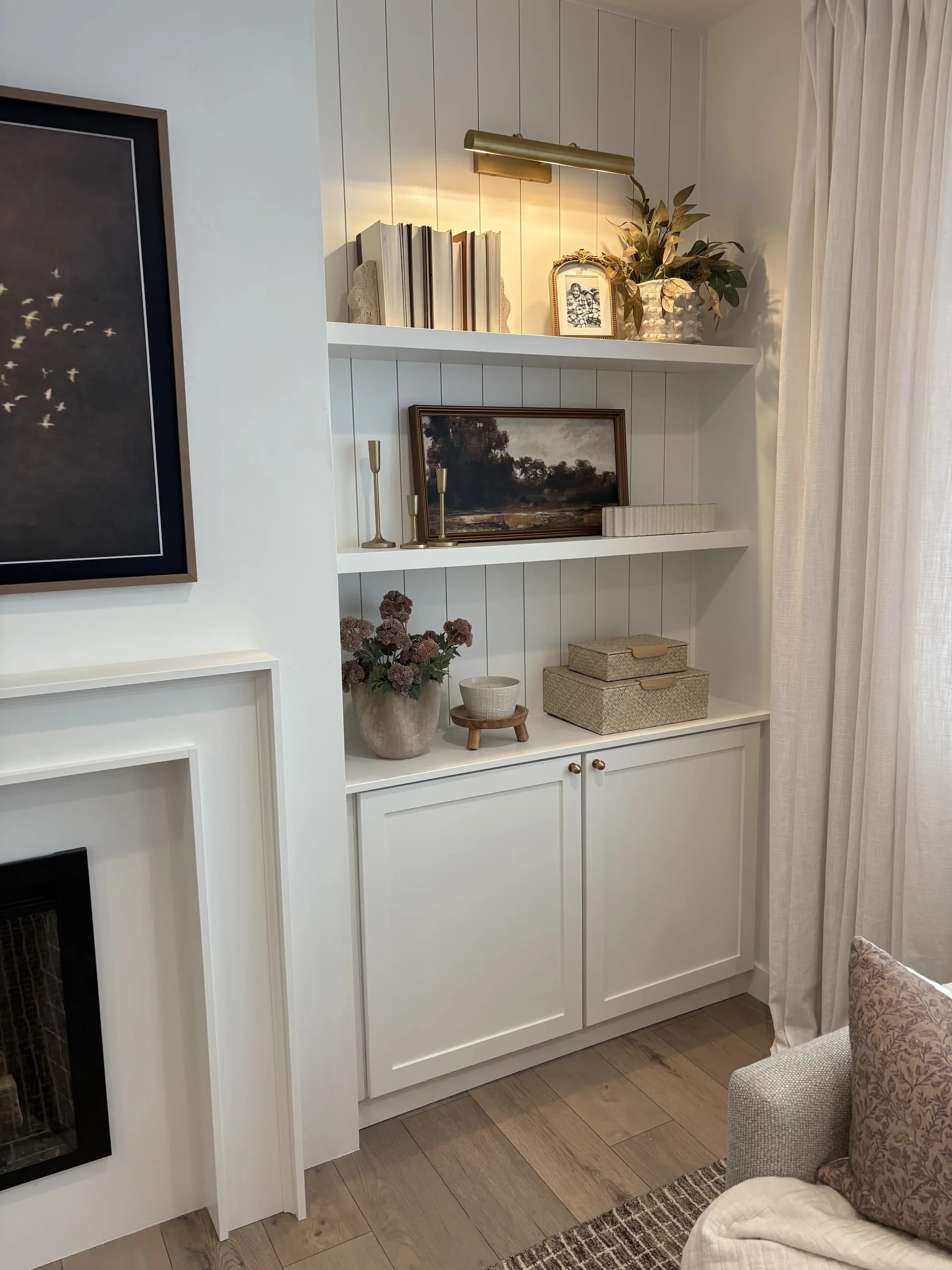 White built-in shelving beside fireplace with brass picture light by BK Toolbox