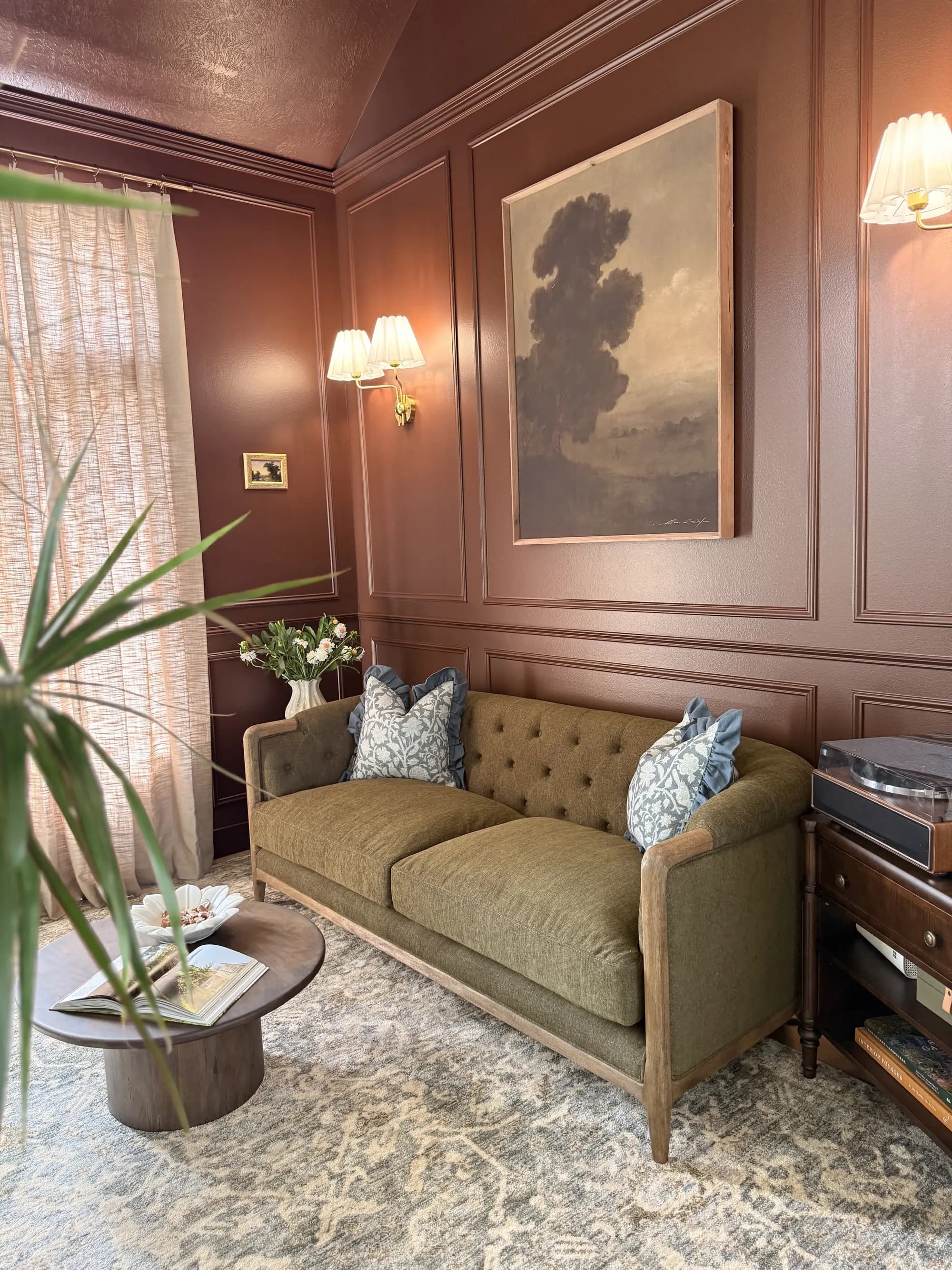 Terracotta paneled study with picture molding, landscape art, and green velvet sofa by BK Toolbox