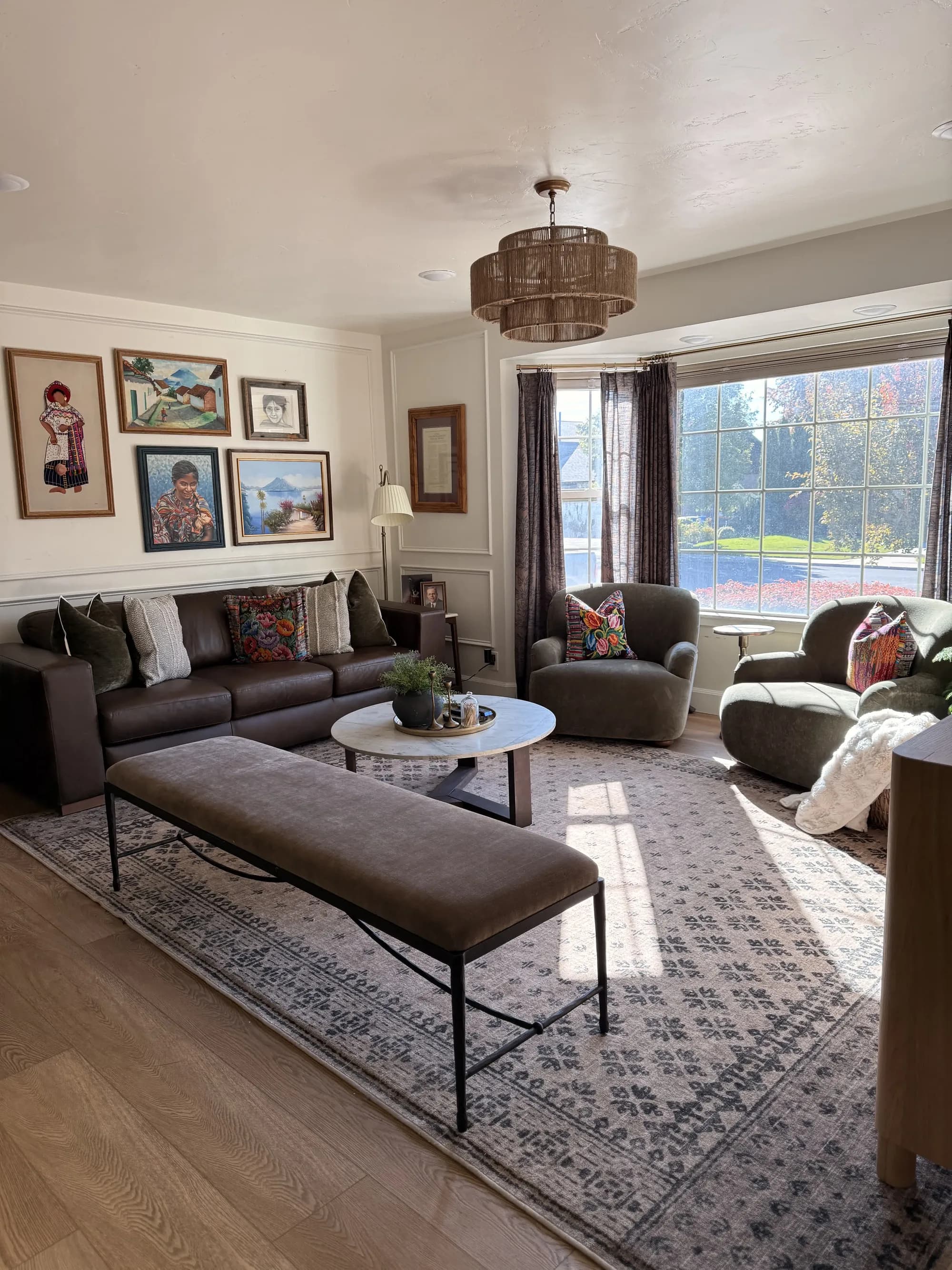 Living room with gallery wall, leather bench, and woven chandelier by BK Toolbox