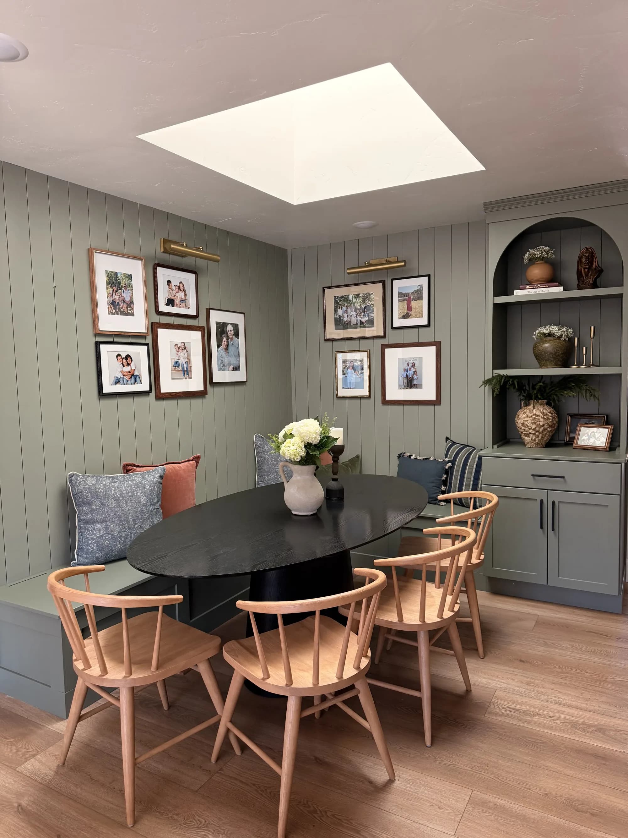 Sage green breakfast nook with built-in banquette, gallery wall, and skylight by BK Toolbox